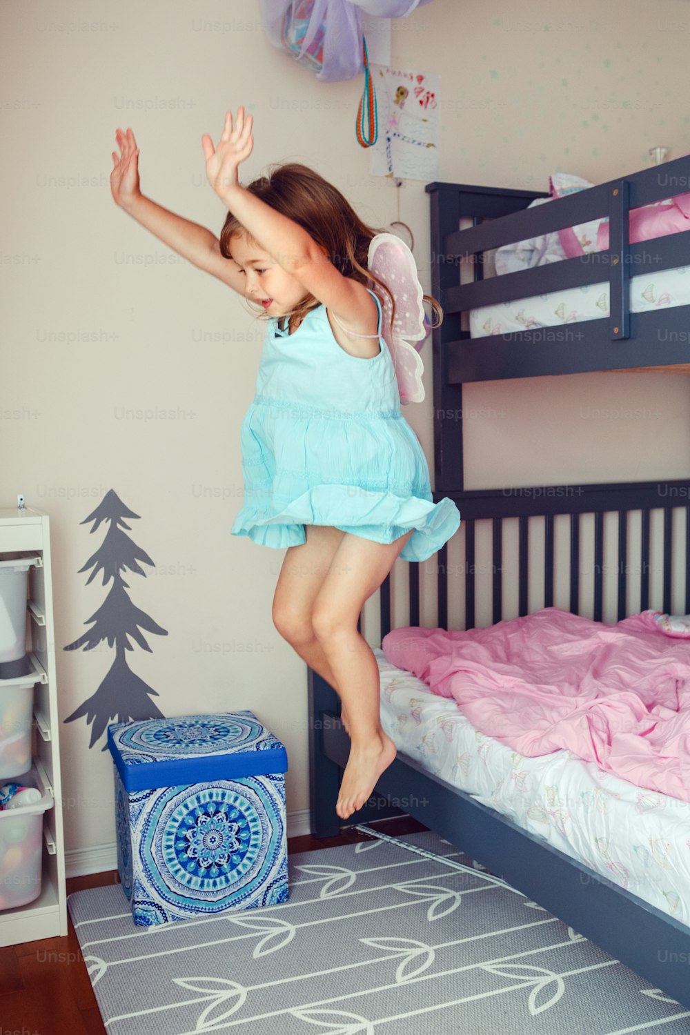 Cute Caucasian girl jumping from bed. Happy excited kid having fun at home. Adorable child playing game flying like elf or fairy. Authentic action candid lifestyle domestic life moment.