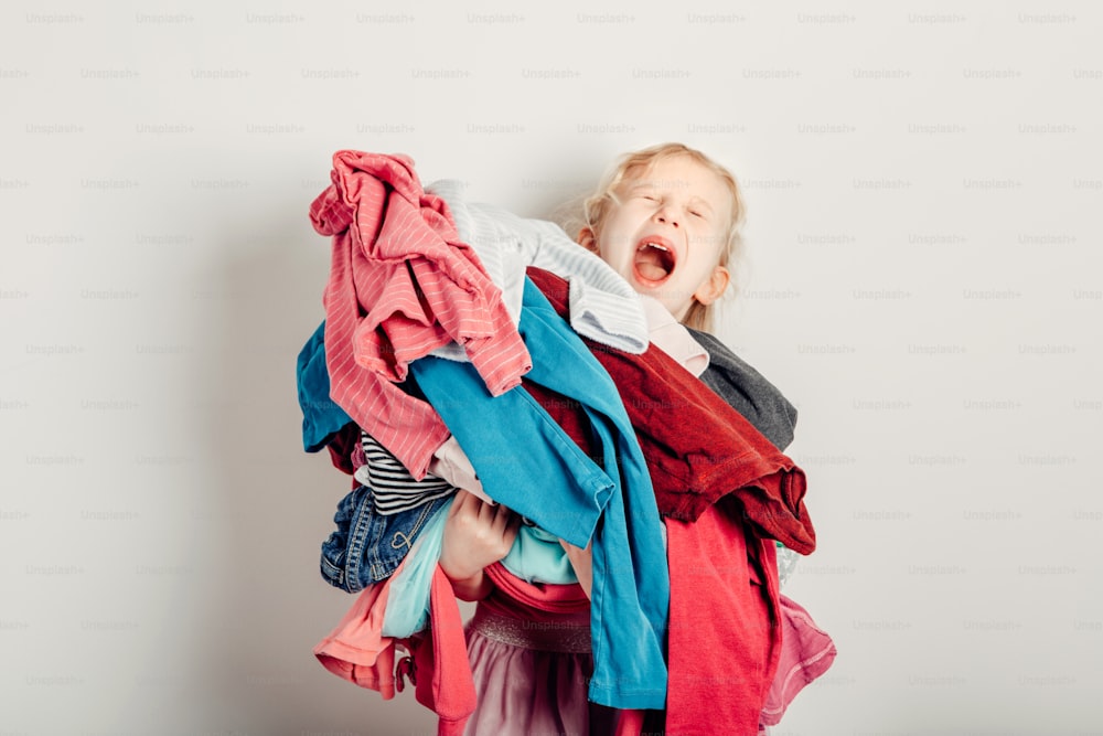 Mommy little helper. Cute Caucasian girl sorting clothes. Adorable funny child arranging organazing clothing. Kid holding messy stack pile of clothes things. Home chores housework.