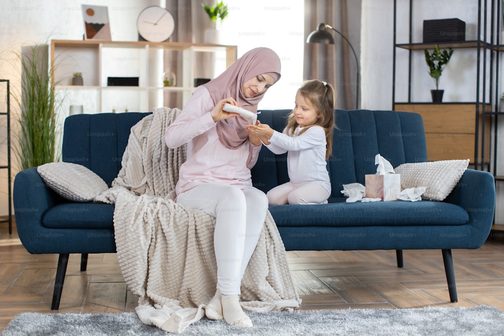 Young Arabian woman in hijab, taking care of her little daughter, applying body lotion or cream on baby hands. Skin home care, children hygiene and healthy lifestyle.