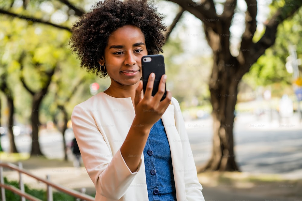 Retrato de una mujer de negocios afro que tiene una videollamada en el teléfono móvil mientras está de pie al aire libre en el parque. Concepto urbano y empresarial.