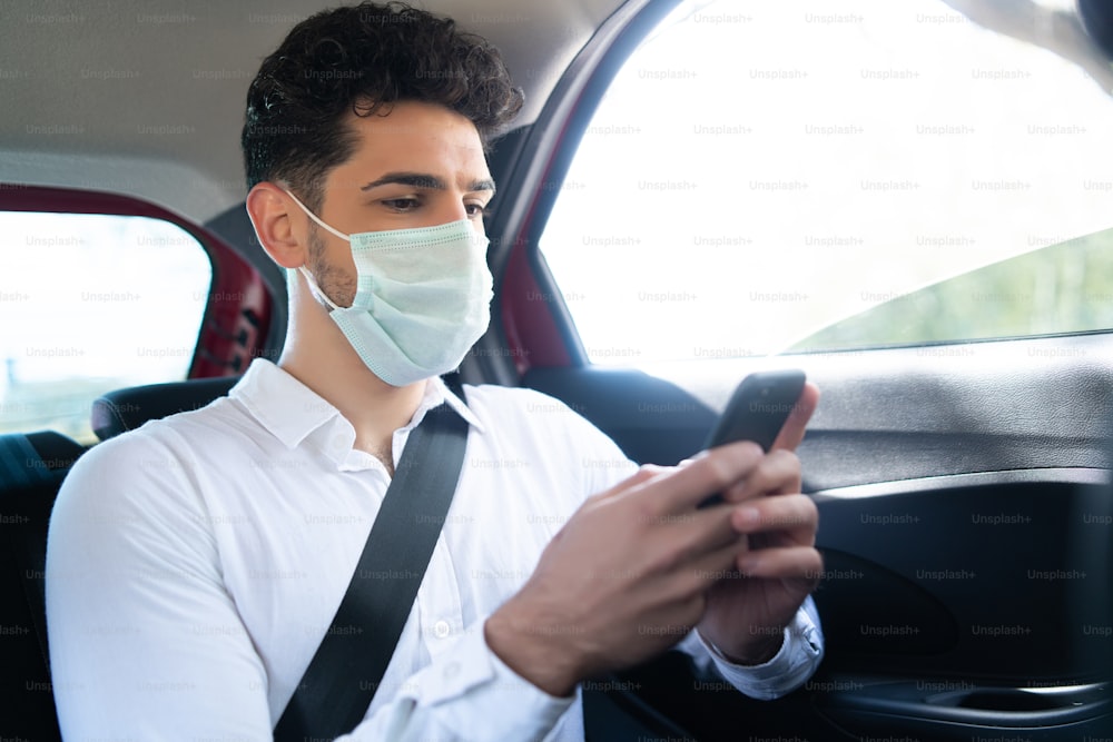 Portrait of businessman wearing face mask and using his mobile phone on way to work in a car. Business concept. New normal lifestyle concept.