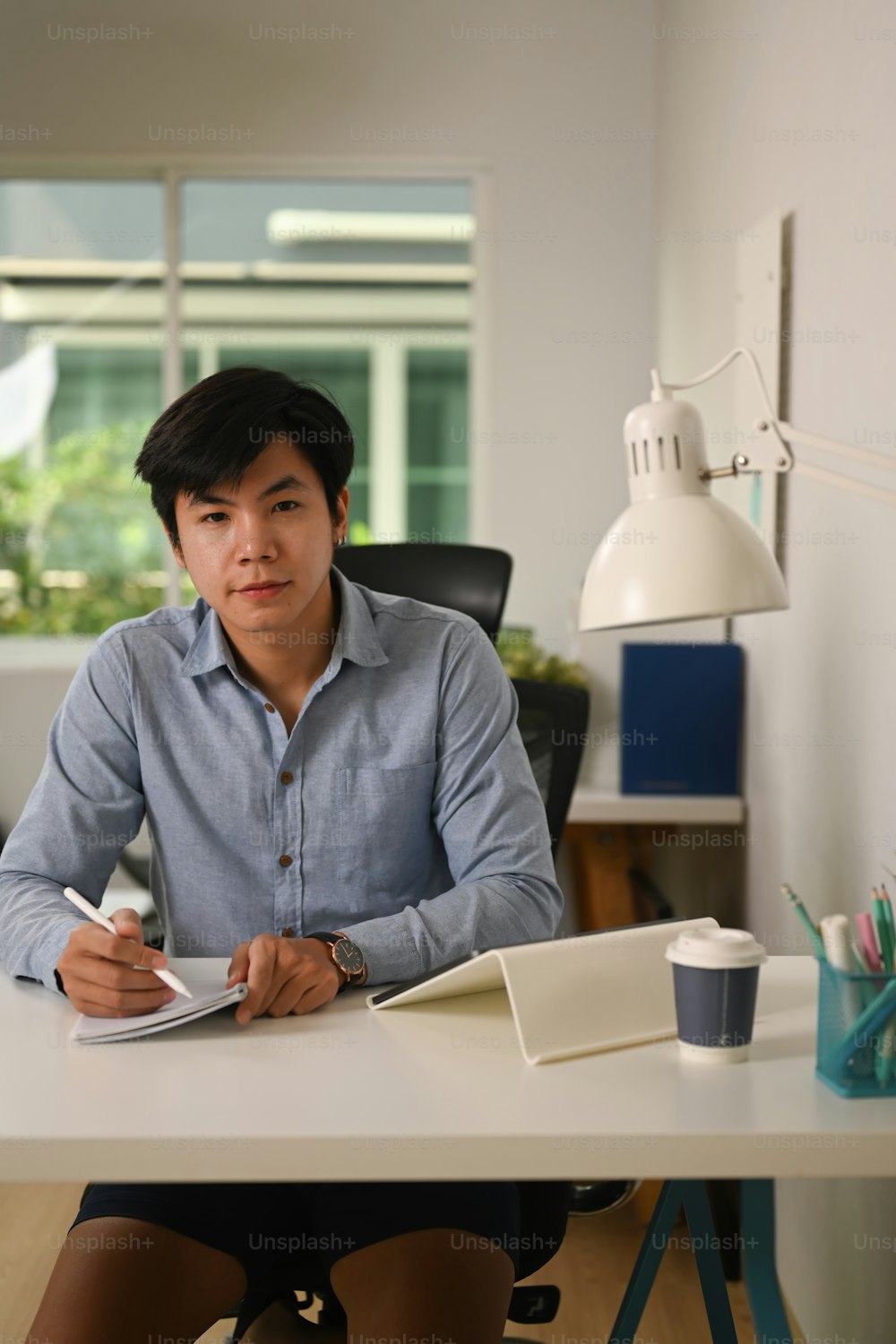 젊은 아시아 사업가의 초상화는 홈 오피스에 앉아 카메라를 보고 있다.