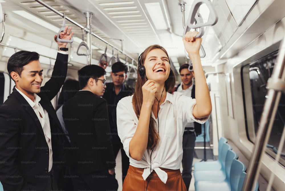 Beautiful young woman passenger standing with headphones and while shirt in the modern subway train