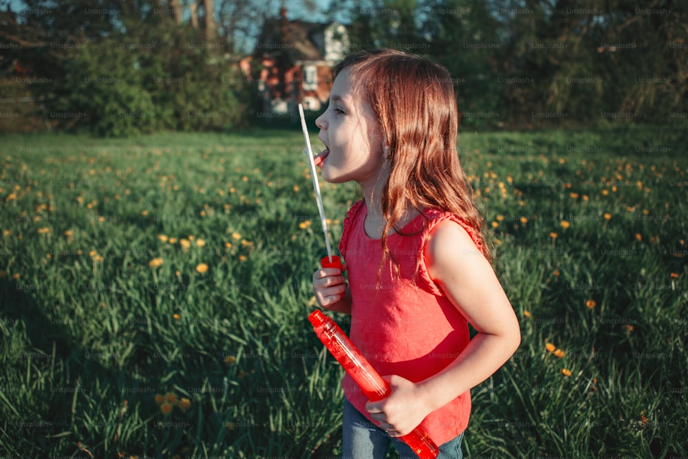Vorschulkaukasisches Mädchen bläst Seifenblasen im Park am Sommertag. Kind hat Spaß im Freien. Authentischer glücklicher magischer Moment der Kindheit. Lifestyle saisonale Aktivität für Kinder.