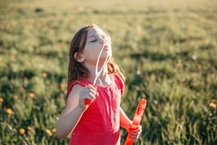 Preschool Caucasian girl blowing soap bubbles in park on summer day. Child having fun outdoor. Authentic happy childhood magic moment. Lifestyle seasonal activity for children.
