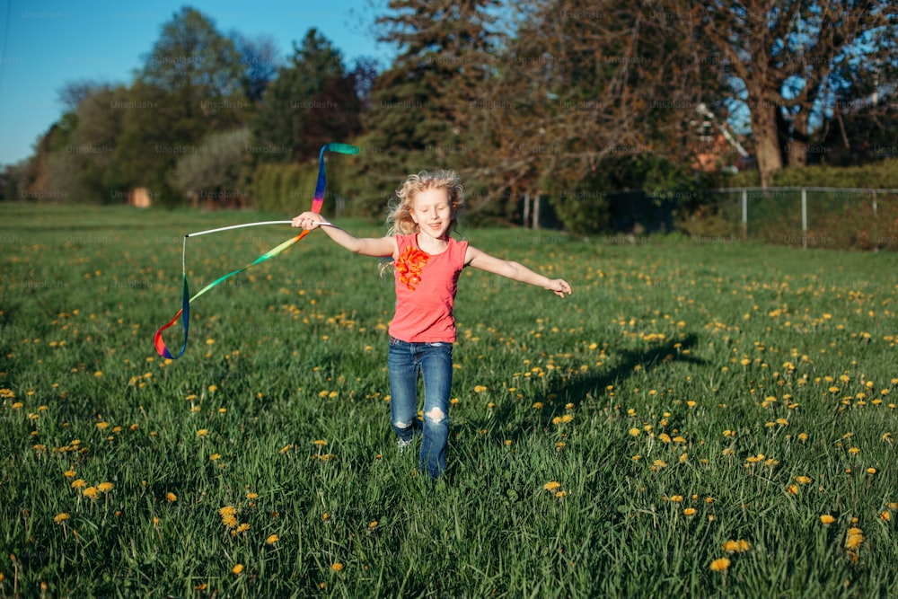 Happy child girl playing with ribbons in park. Cute adorable kid running on meadow playing together. Outdoor summer backyard activity for kids. Innocent childhood candid authentic lifestyle.