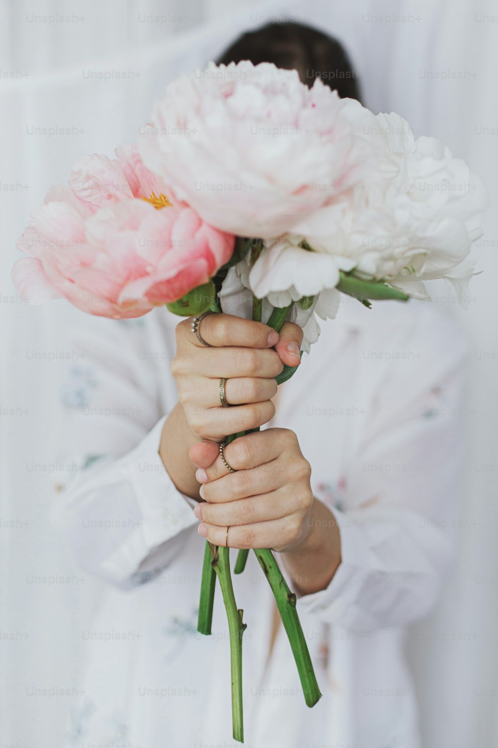 Beautiful stylish woman holding peony bouquet in hands. Young female hiding behind big pink and white peony flowers. Sensual soft image. Spring aesthetics. Wedding bouquet