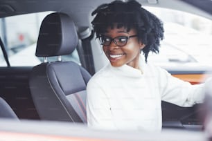 Joven mujer afroamericana se sienta dentro de un nuevo coche moderno.