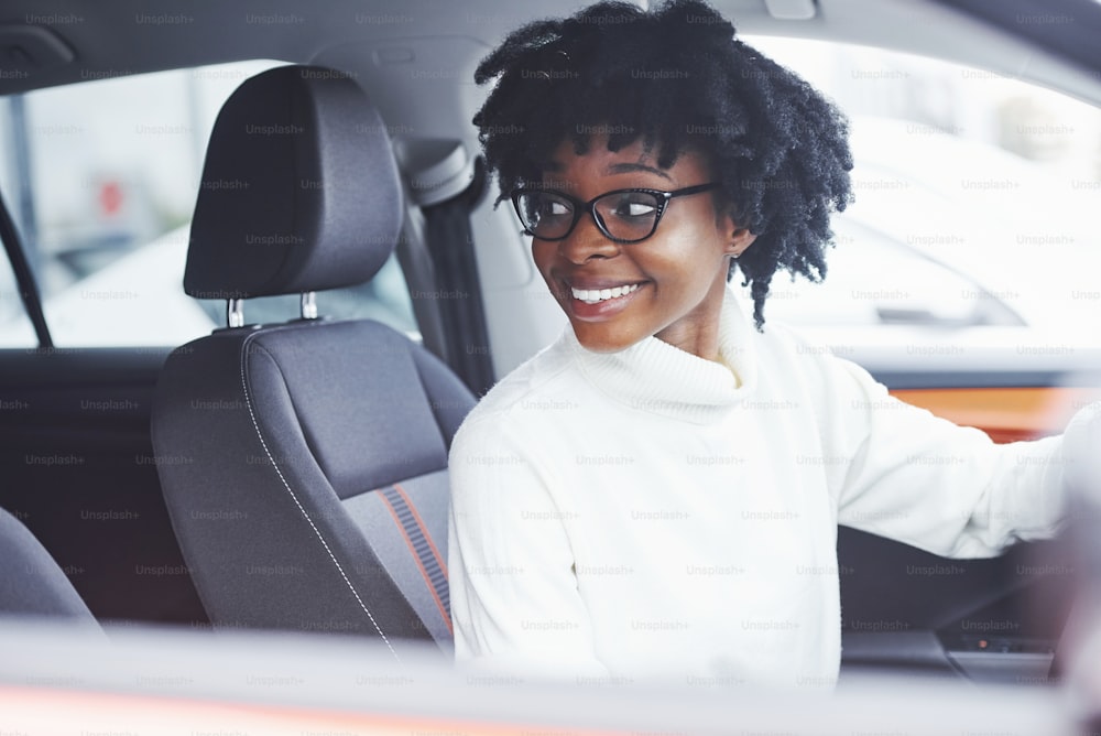 Mulher afro-americana jovem senta-se dentro do carro moderno novo.