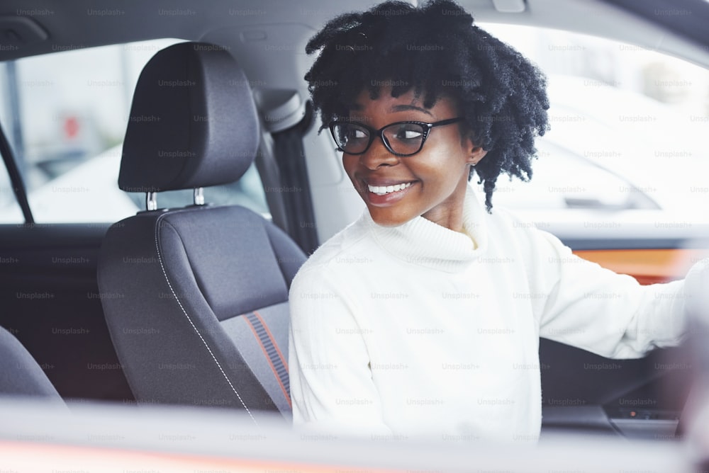 Young african american woman sits inside of new modern car.