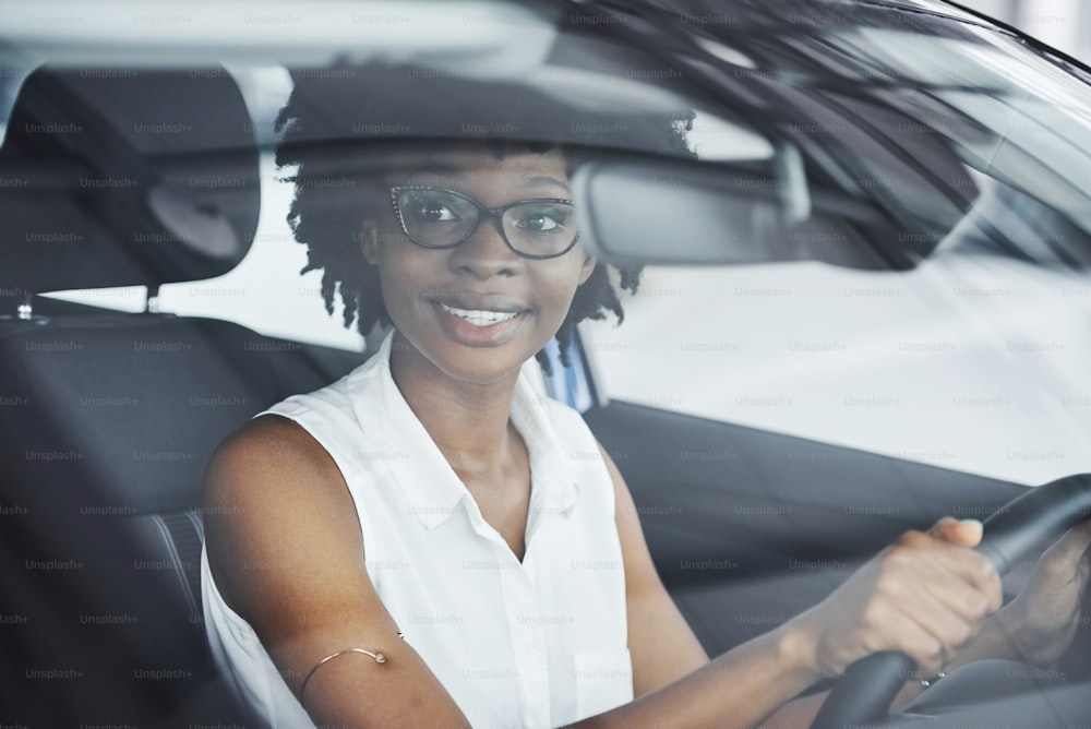 Giovane donna afroamericana si siede all'interno di una nuova auto moderna.