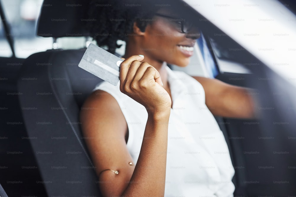 신용 카드를 보유합니다. 젊은 아프리카 계 미국인 여성이 새로운 현대 자동차 안에 앉아 있습니다.