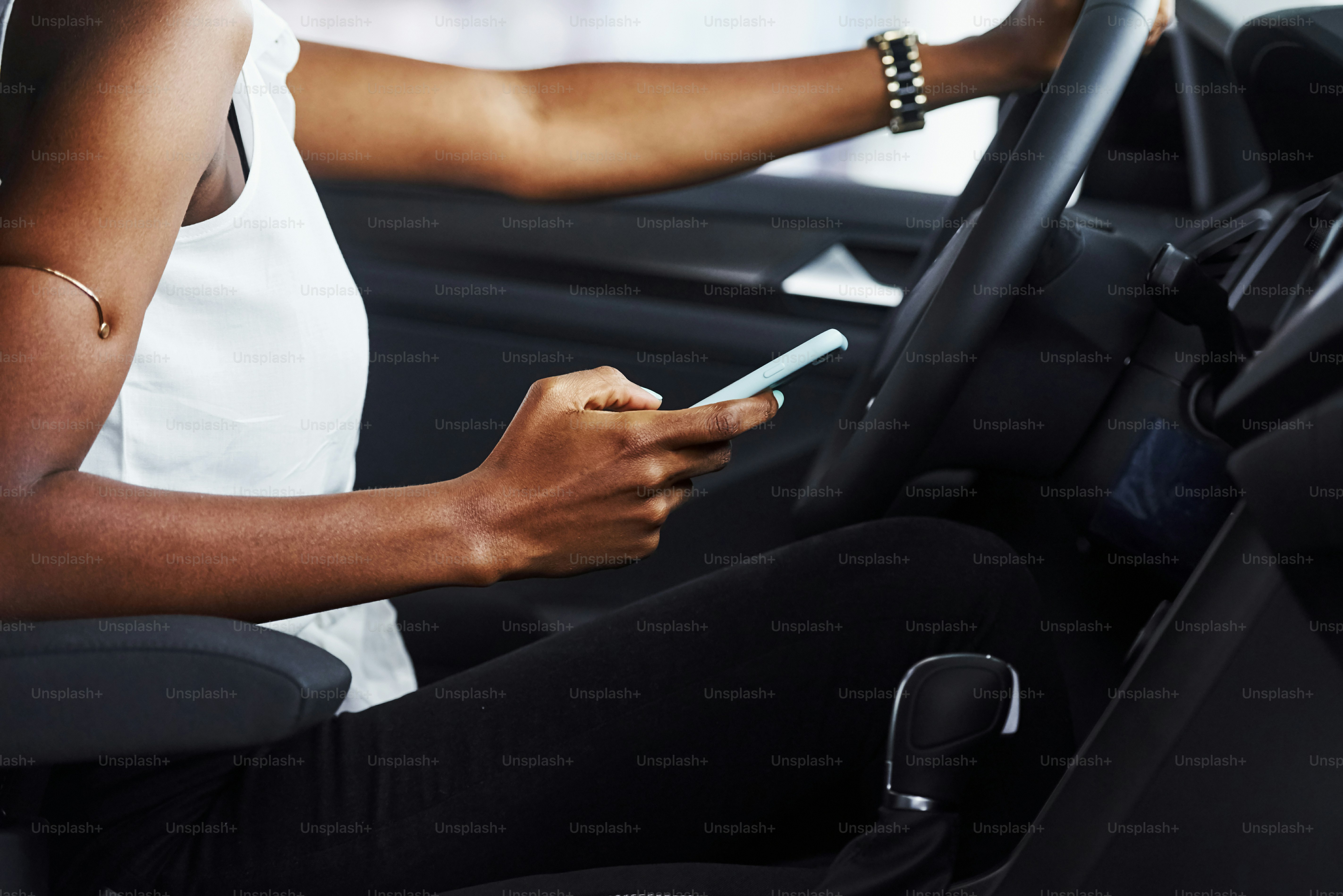 Particle view of young african american woman that sits inside of new modern car with phone in hand.