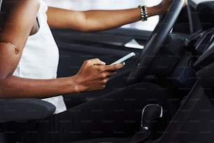 Particle view of young african american woman that sits inside of new modern car with phone in hand.