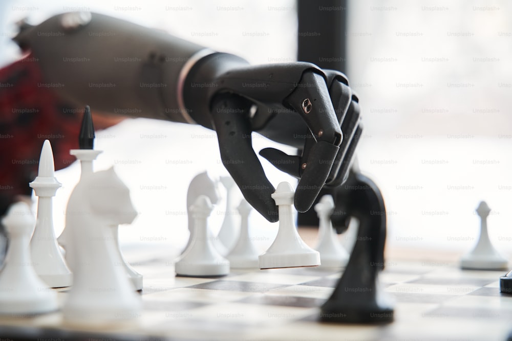 Male engineer holding chess piece with black bionic hand while playing at the chess and testing limb at his workplace. Engineering of the bionic hands concept. Stock photo