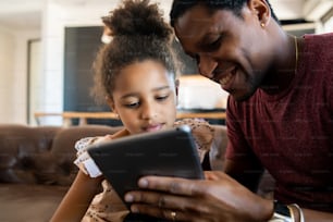 Porträt einer Tochter und eines Vaters, die zu Hause Spaß haben und mit dem digitalen Tablet spielen. Monoparentales Konzept.