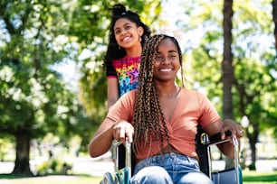 An african american woman in a wheelchair enjoying a walk at the park with her daughter.