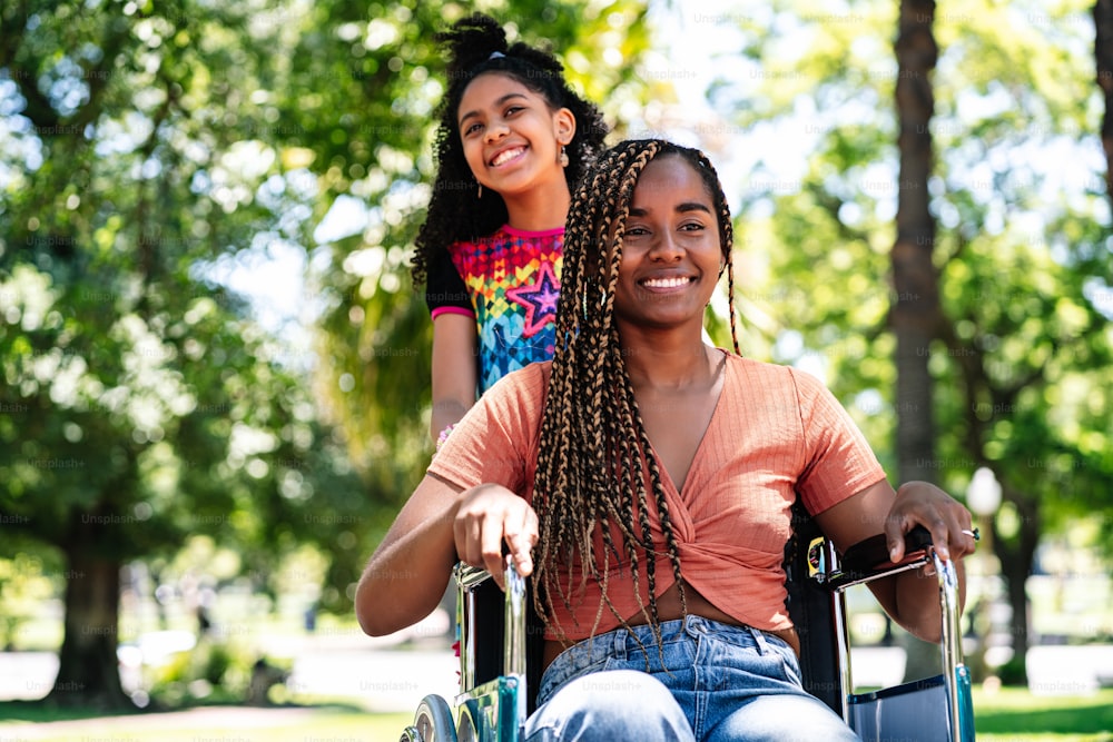 휠체어를 탄 아프리카계 미국인 여성이 딸과 함께 공원에서 산책을 즐기고 있다.