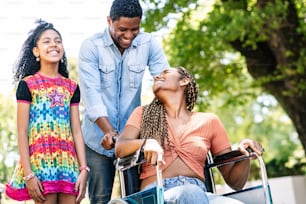 An african american woman in a wheelchair enjoying a walk outdoors with her daughter and husband.