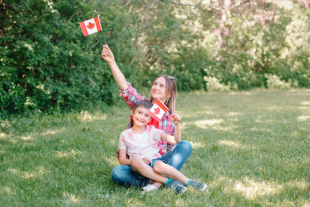 Mamma di famiglia con figlio che celebra la Giornata nazionale del Canada il 1 ° luglio. Madre caucasica con bambino che sventola bandiere canadesi. I cittadini orgogliosi celebrano il Canada Day nel parco all'aperto.