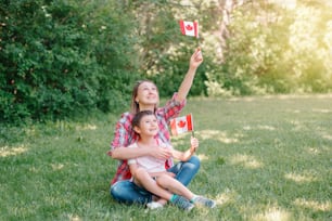 Family mom with son celebrating national Canada Day on 1st of July. Caucasian mother with child boy waving Canadian flags. Proud citizens celebrate Canada Day in park outdoor.