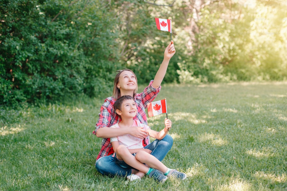 Mãe de família com filho comemorando o Dia Nacional do Canadá em 1º de julho. Mãe caucasiana com menino acenando bandeiras canadenses. Cidadãos orgulhosos celebram o Dia do Canadá no parque ao ar livre.
