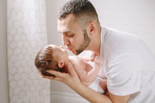 Happy young Caucasian father kissing newborn baby. Dad man parent holding rocking child daughter son on his hands. Authentic lifestyle candid family moment.  Fathers Day holiday.