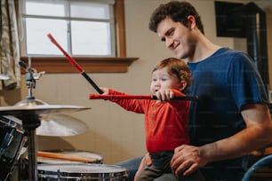 Vater bringt dem kleinen Jungen das Schlagzeugspielen bei. Eltern mit Kleinkind haben Spaß und verbringen Zeit miteinander. Papa und Kind beim Musizieren. Familienhobby und Freizeit während der Selbstisolation.