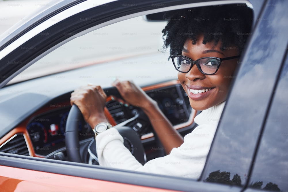 Mulher afro-americana jovem senta-se dentro do carro moderno novo.