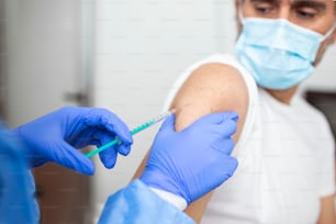 Gros plan sur le médecin tenant une seringue et utilisant du coton avant de faire l’injection au patient dans un masque médical. Vaccin contre le Covid-19 ou le coronavirus