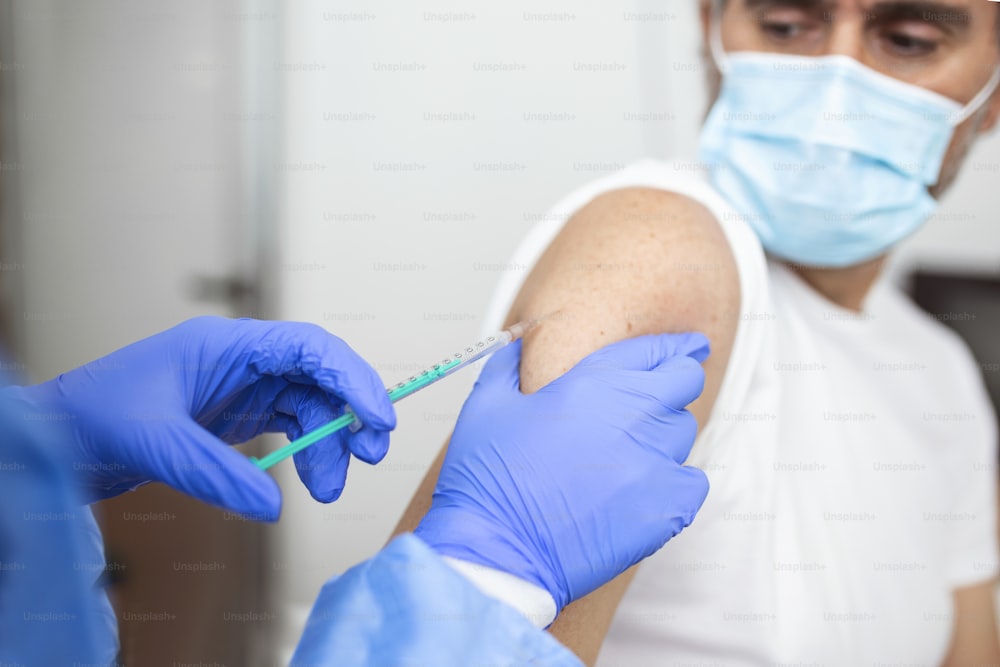 Nahaufnahme Arzt hält Spritze und verwendet Baumwolle vor der Injektion an den Patienten in medizinischer Maske. Covid-19- oder Coronavirus-Impfstoff
