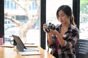 Young woman photographer or designer checking photo on her camera and working with computer tablet at office.
