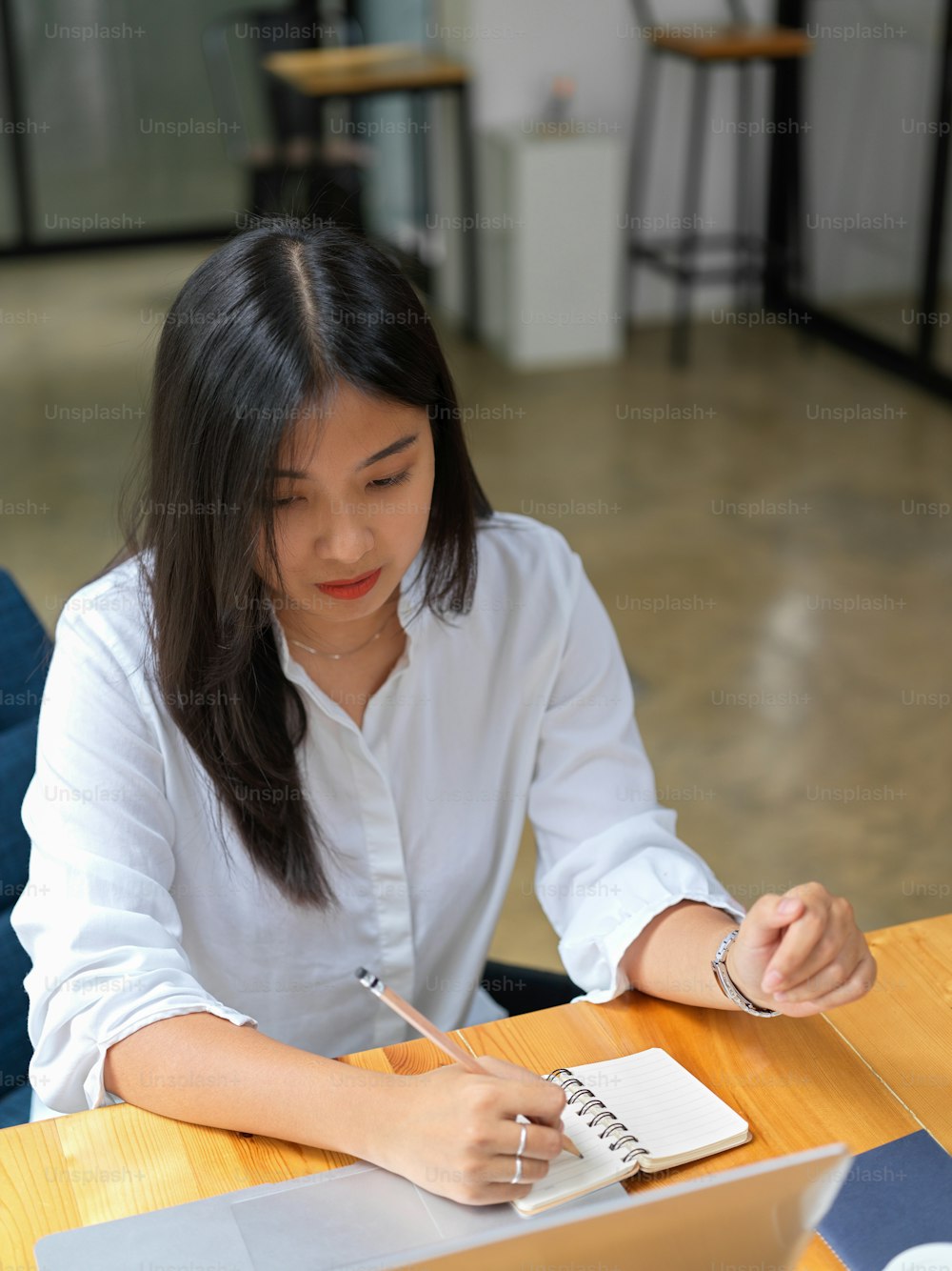 Colpo ritagliato di una lavoratrice che scrive su un taccuino bianco mentre lavora con il computer portatile sul tavolo di legno