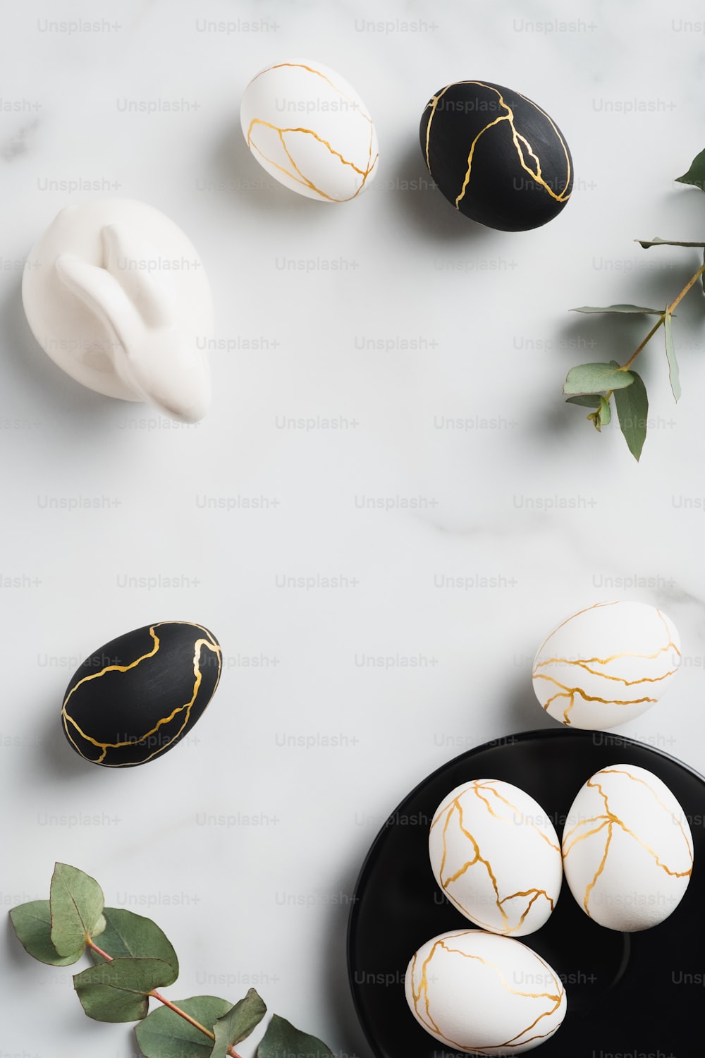 Luxury Easter eggs decorated gold, Easter bunny, eucalyptus on marble table. Flat lay, top view, vertical.