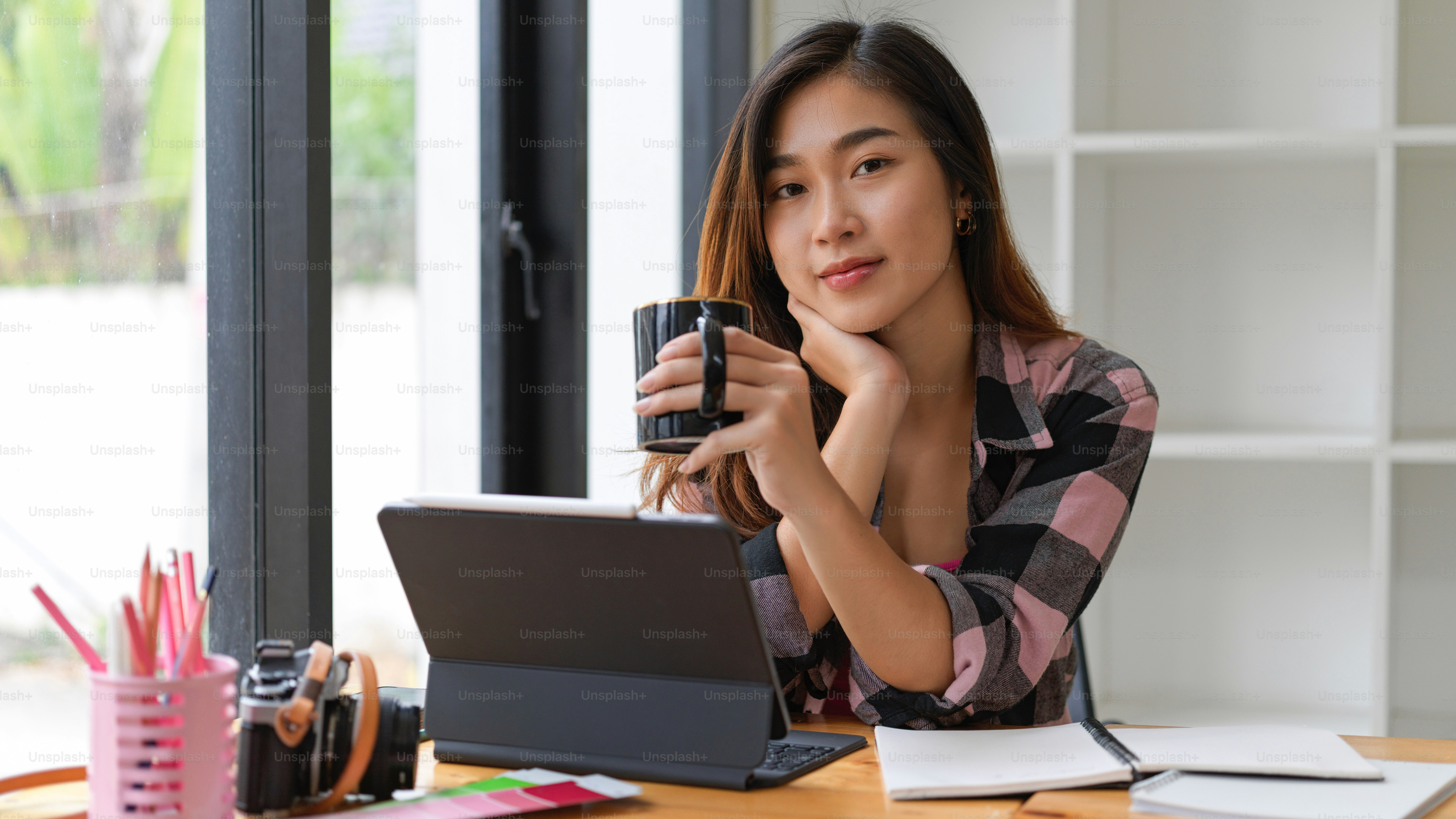 Portrait of female student smiling to camera while drinking coffee break while doing assignment in living room