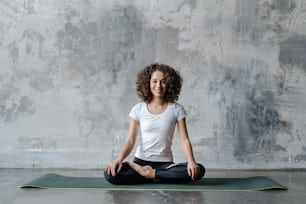 Happy and young african american woman sitting in meditation pose, doing yoga training on exercise mat. Adult female in sportswear make zen practice before workout in fitness center