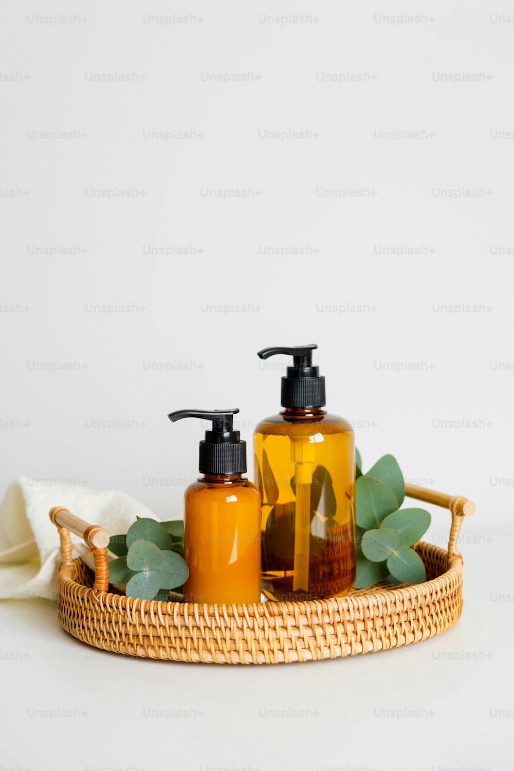 Rattan tray with amber glass pump bottles of shampoo or shower gel, eucalyptus plant branches, towel. SPA natural organic cosmetics set on table in bathroom.
