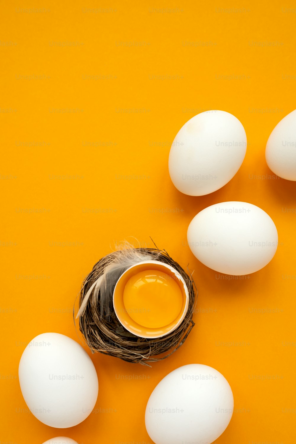 Uova bianche e tuorlo d'uovo nel nido su sfondo giallo. Vista dall'alto. Posa piatta. Celebrazione della Pasqua
