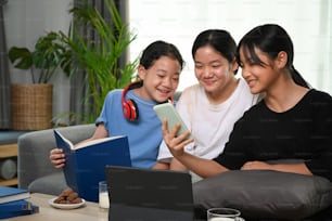 Tres chicas asiáticas divirtiéndose el fin de semana usando un teléfono inteligente y sentadas en el sofá de casa.