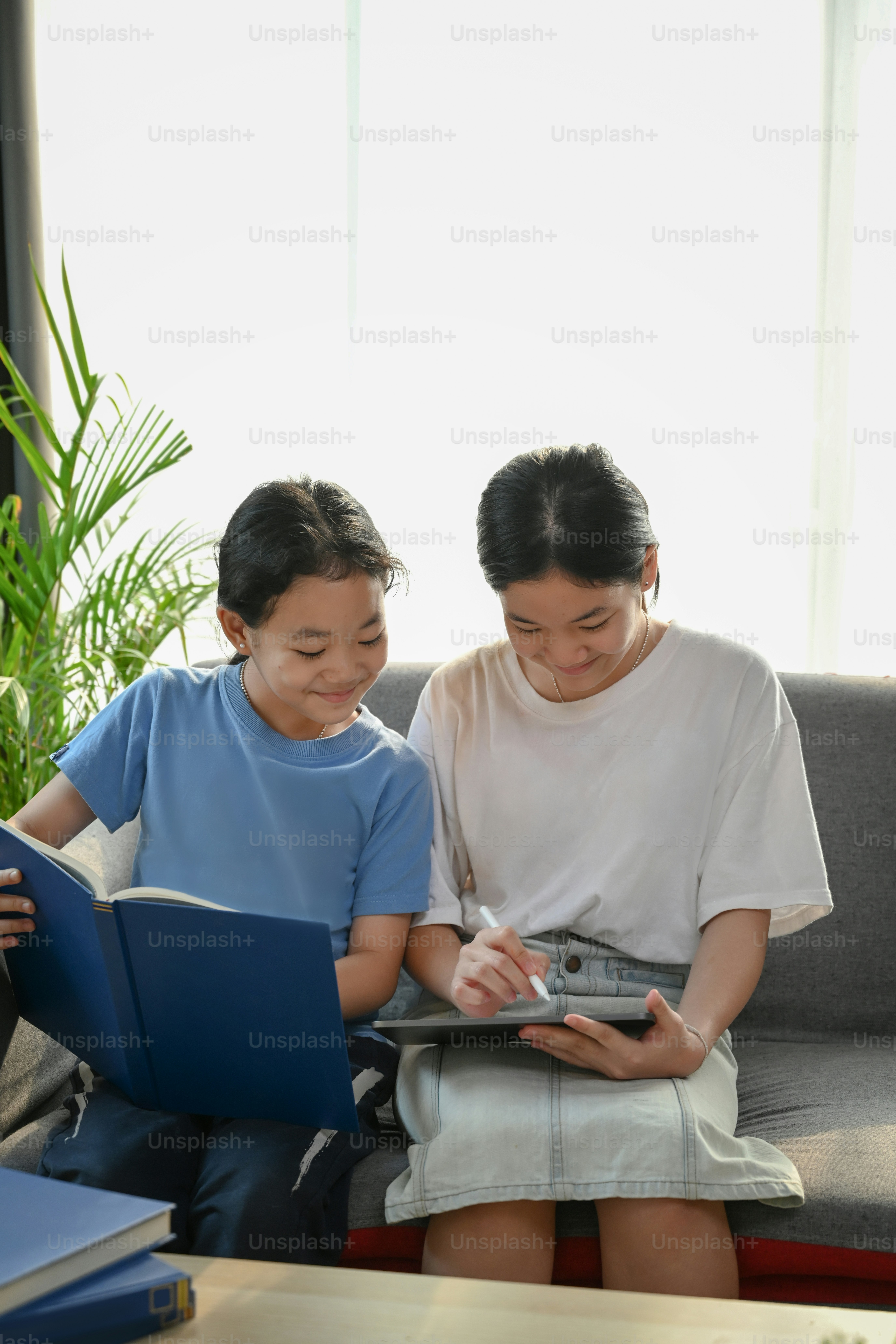 Two happy asian girl using digital tablet together and siting on sofa ...