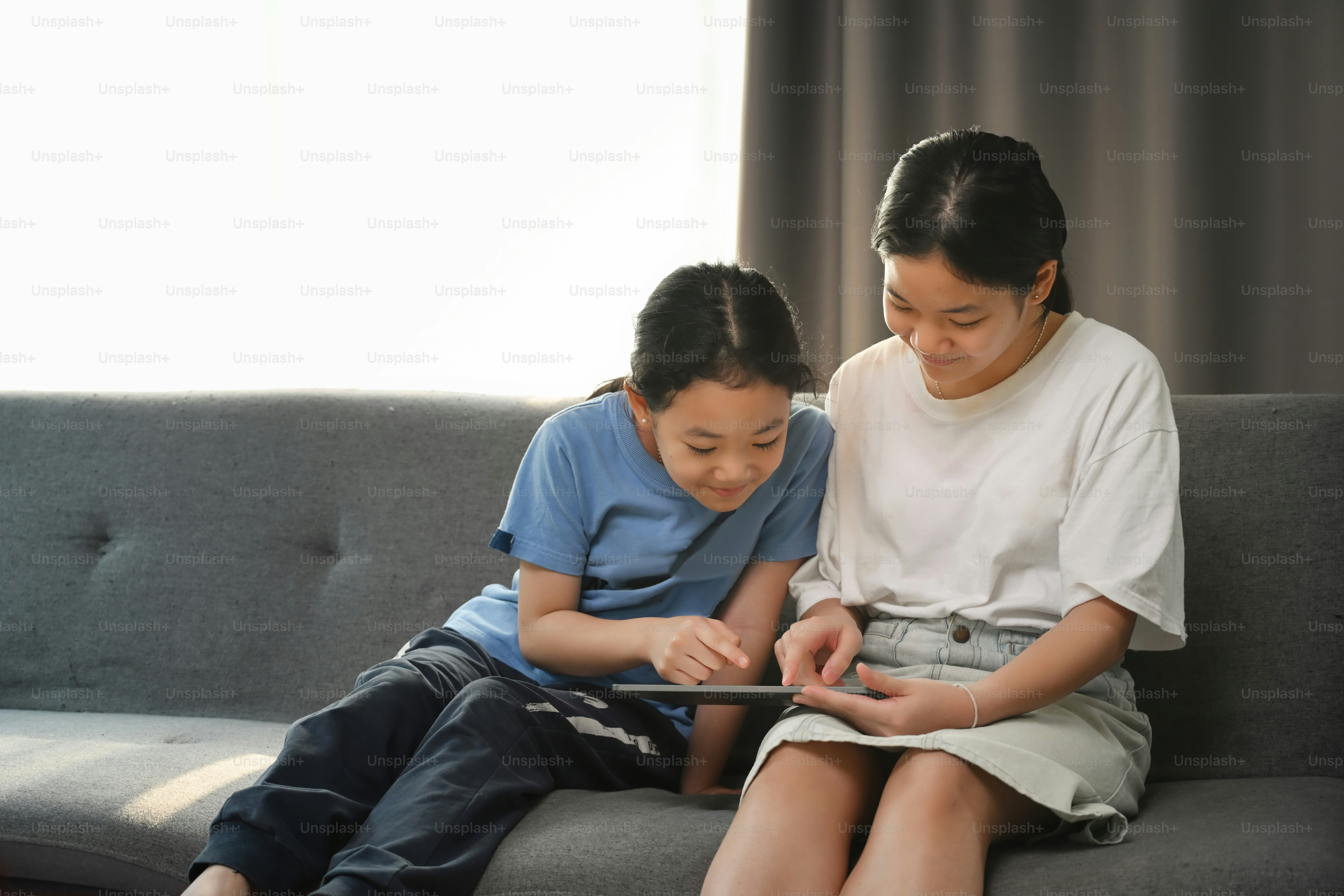 Young asian girl sitting on sofa in living room using computer tablet ...