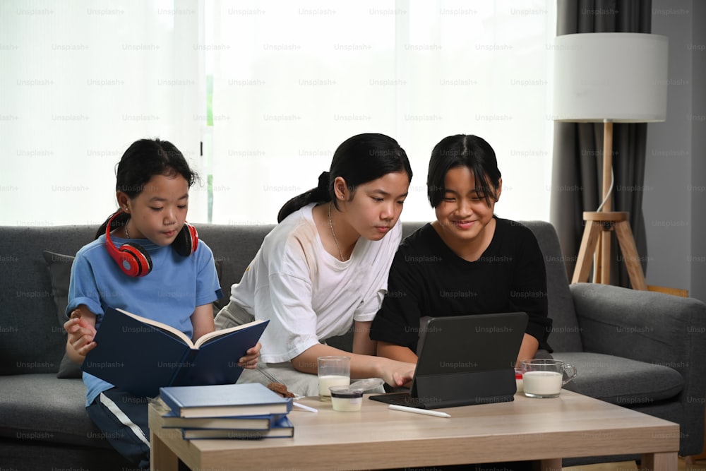 세 명의 아시아 소녀가 소파에 앉아 디지털 태블릿을 사용하고 있다.
