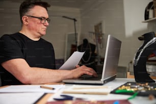 Portrait of a serious man with a sheet of paper in his hand typing on his laptop