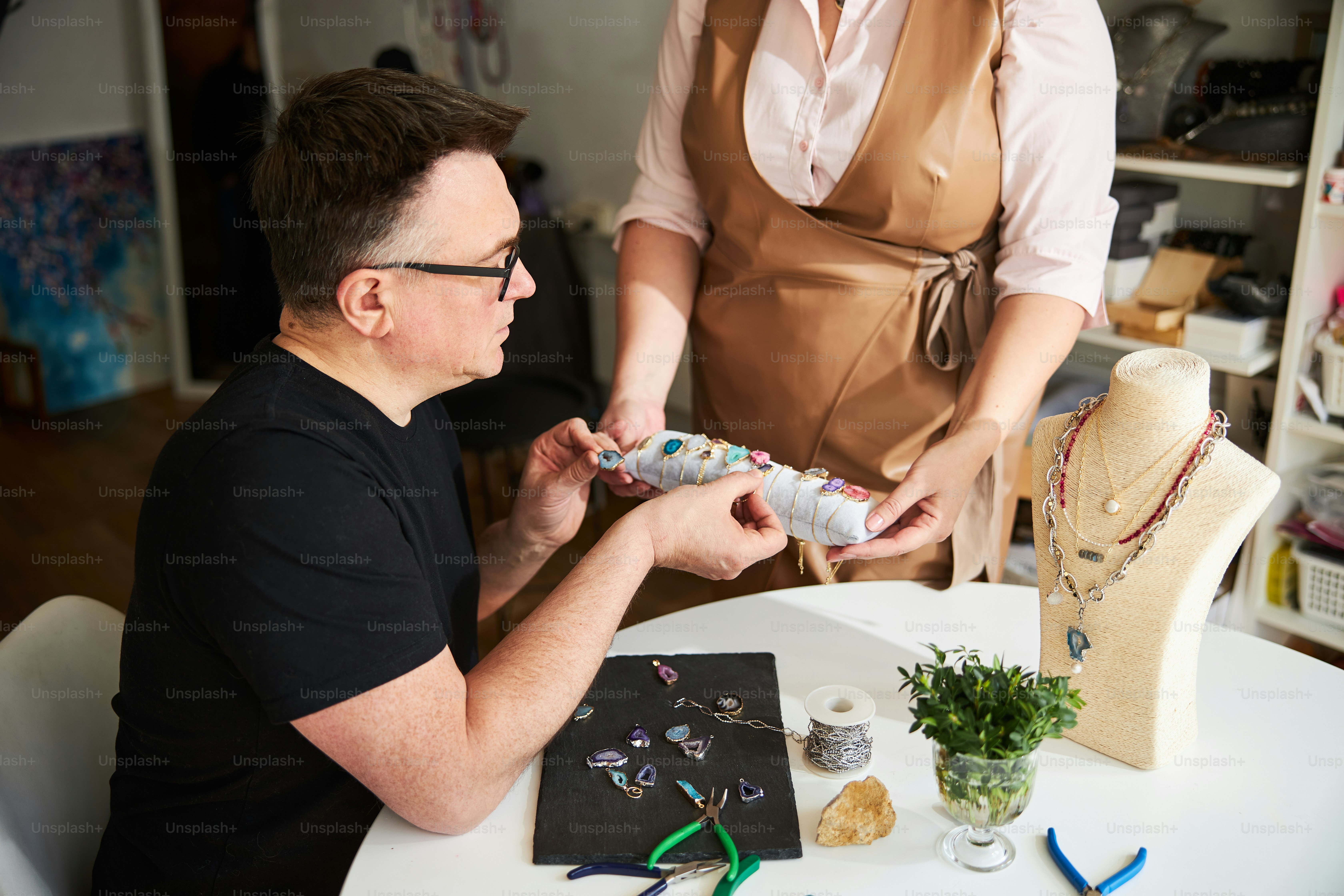 Artisan concentré dans les lunettes choisissant les bons bracelets pour ses boucles d’oreilles sur le coussin de présentation de bijoux