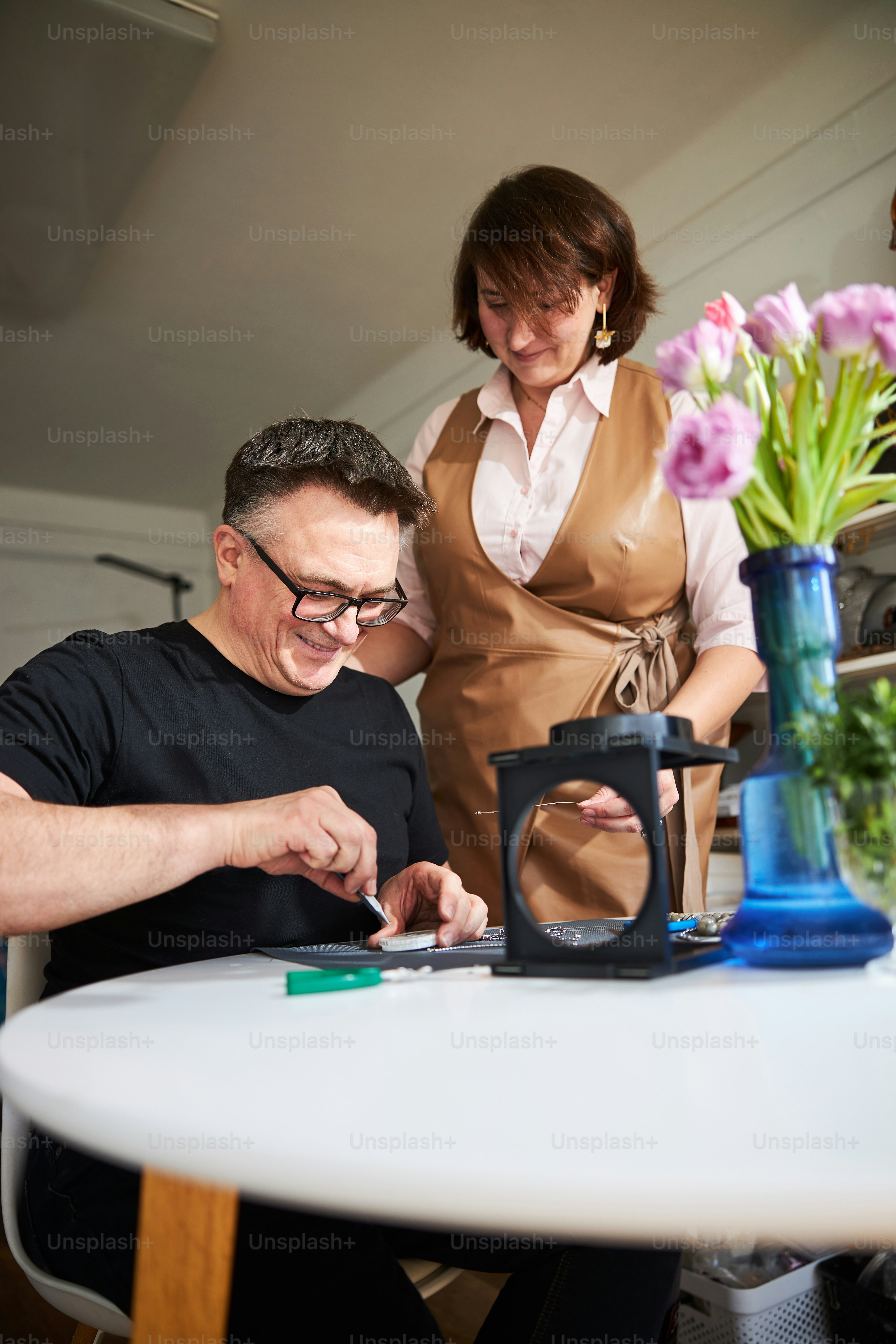 Mujer mirando a un joyero sonriente recogiendo un detalle de una caja de plástico con un par de pinzas