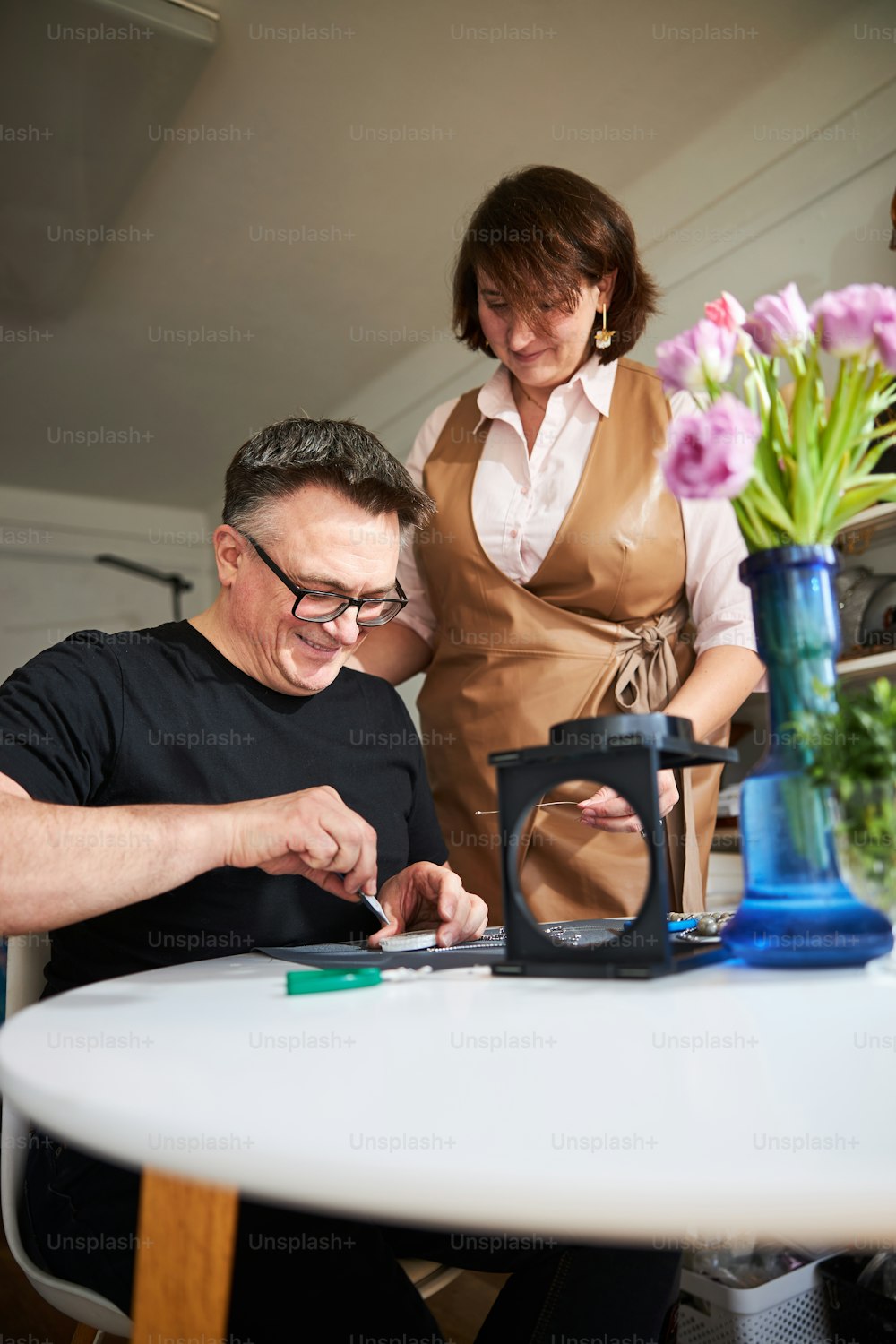 Woman watching a smiling jeweler picking up a detail from a plastic box with a pair of tweezers