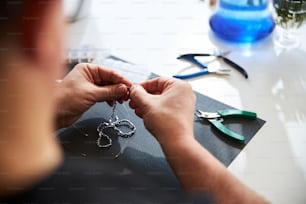 Foto ritagliata di un artigiano esperto che realizza una chiusura per una collana seduta al tavolo
