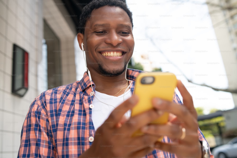 笑顔で携帯電話を使っているアフリカ系アメリカ人の男性が、屋外の路上に立っています。アーバンコンセプト。