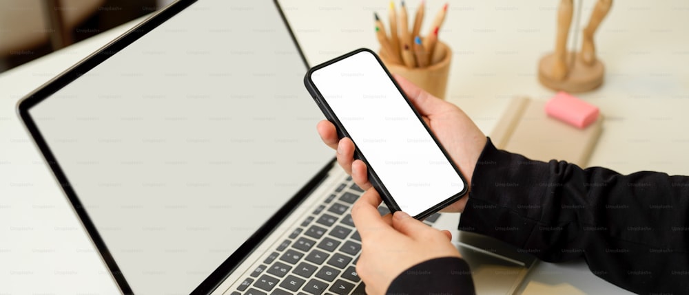 Close up view of female in blank jacket hand holding smartphone include clipping path screen on workspace