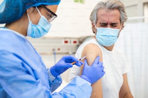 Professional doctor or nurse giving flu or COVID-19 injection to patient. Man in medical face mask getting antiviral vaccine at hospital or health center during vaccination and immunization campaign